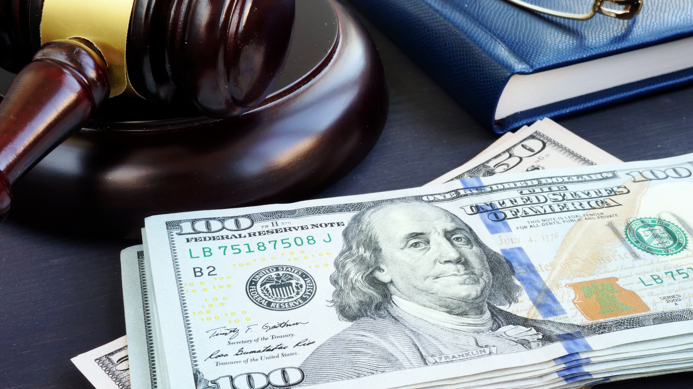 Close up of judge's gavel, corner of a blue book, and a stack of Benjamins.
